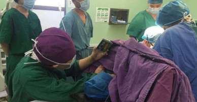 Y tá ân cần quỳ bên bàn mổ suốt cả tiếng đồng hồ để cầm điện thoại cho bệnh nhi xem hoạt hình